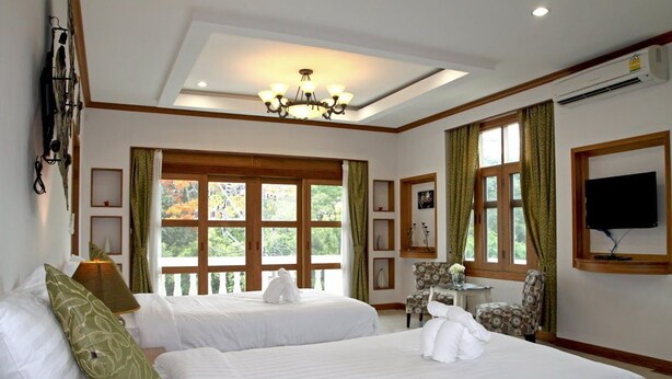 Habitación de hotel con dos camas, un candelabro, un televisor y ventanas amplias con cortinas.