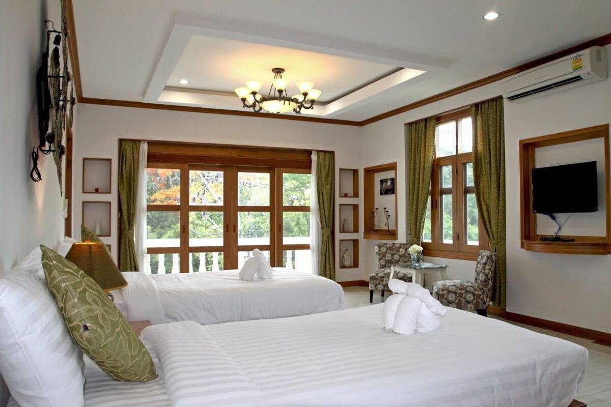 Une chambre d’hôtel avec deux lits, un lustre, une télévision et de grandes fenêtres avec des rideaux.