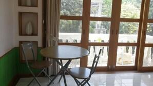 Un comedor con una mesa redonda y dos sillas, un armario de madera con un jarrón, y un ventanal con vistas a vegetación y un edificio.
