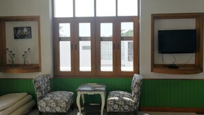 Una habitación con un ventanal grande, dos sillones estampados, una mesita, un sofá y un televisor montado en la pared.