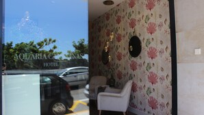 A hotel lobby with a floral wallpaper, a white armchair, and a round mirror on the wall. - Hotel Aquaria Caneliñas (Sanxenxo)