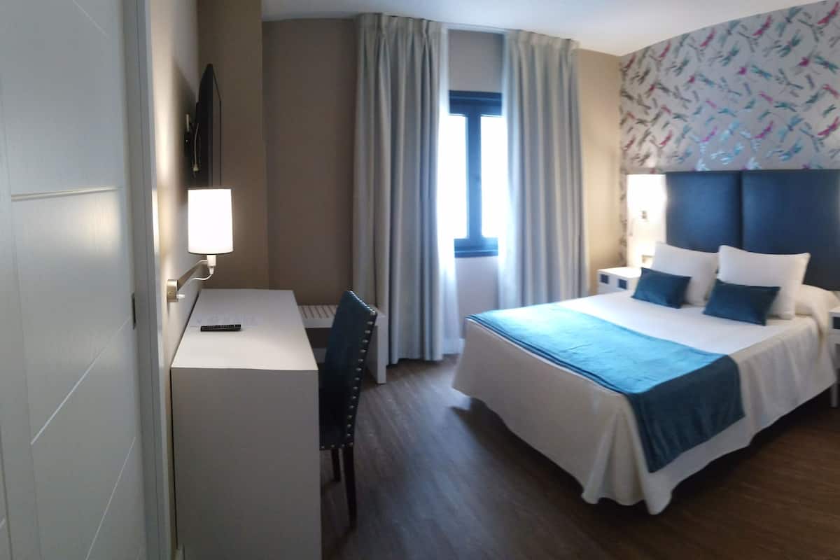 Ein Hotelzimmer mit Bett, Nachttischen, Schreibtisch, Stuhl, Fenster mit Vorhängen und einer Wand mit Muster.
