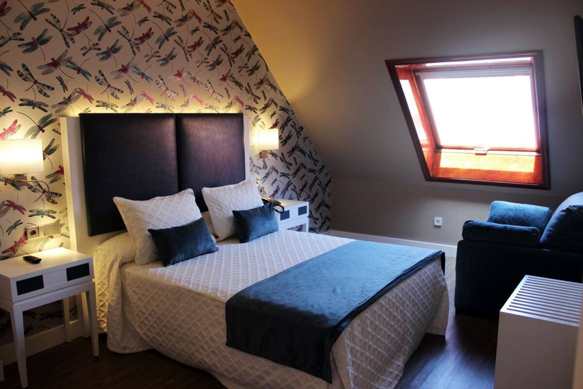 Ein Schlafzimmer mit Bett, Nachttischen, Fenster und einem Sessel.
