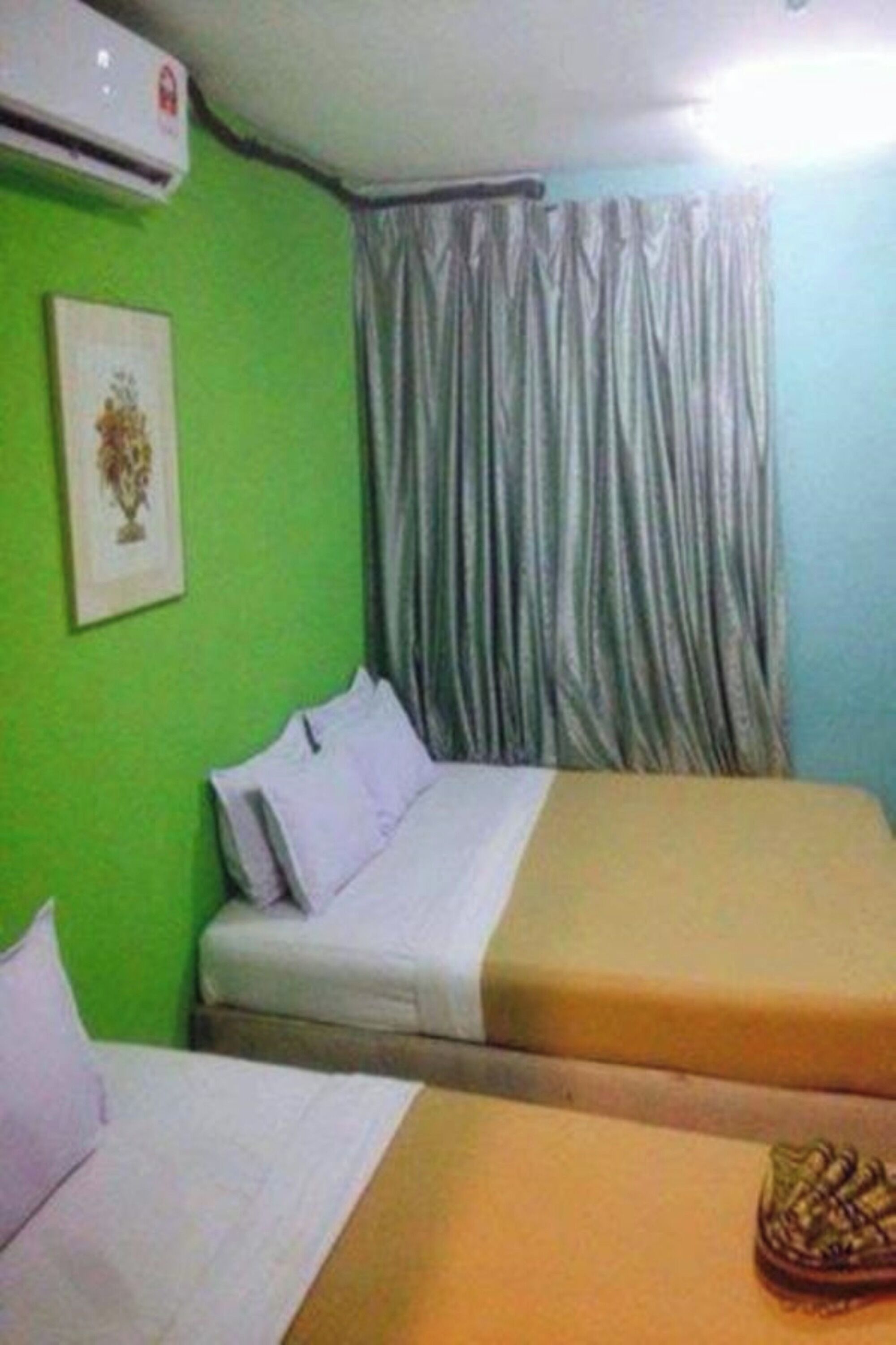 A room with two beds, a green wall, a framed picture, and a window with curtains.