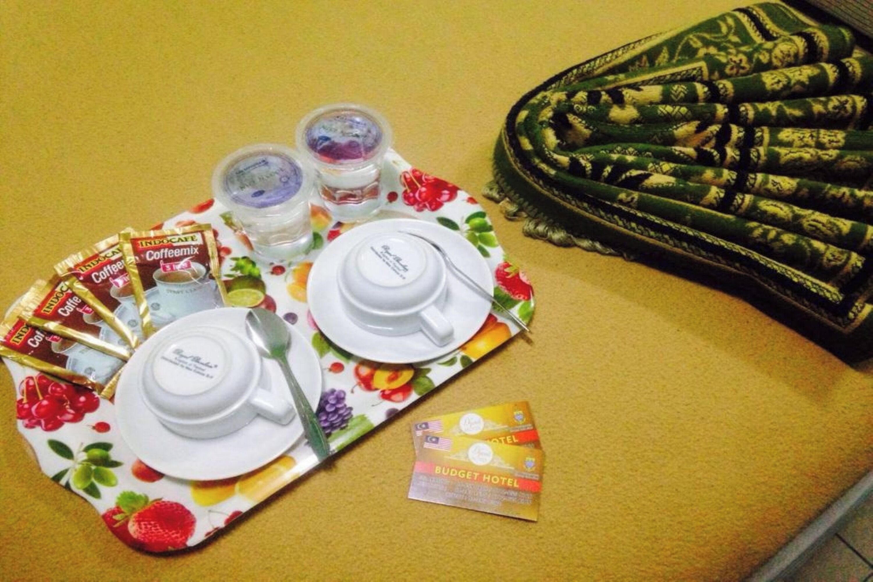 Una bandeja con sobres de café, un juego de té y un folleto del hotel sobre una superficie amarilla.