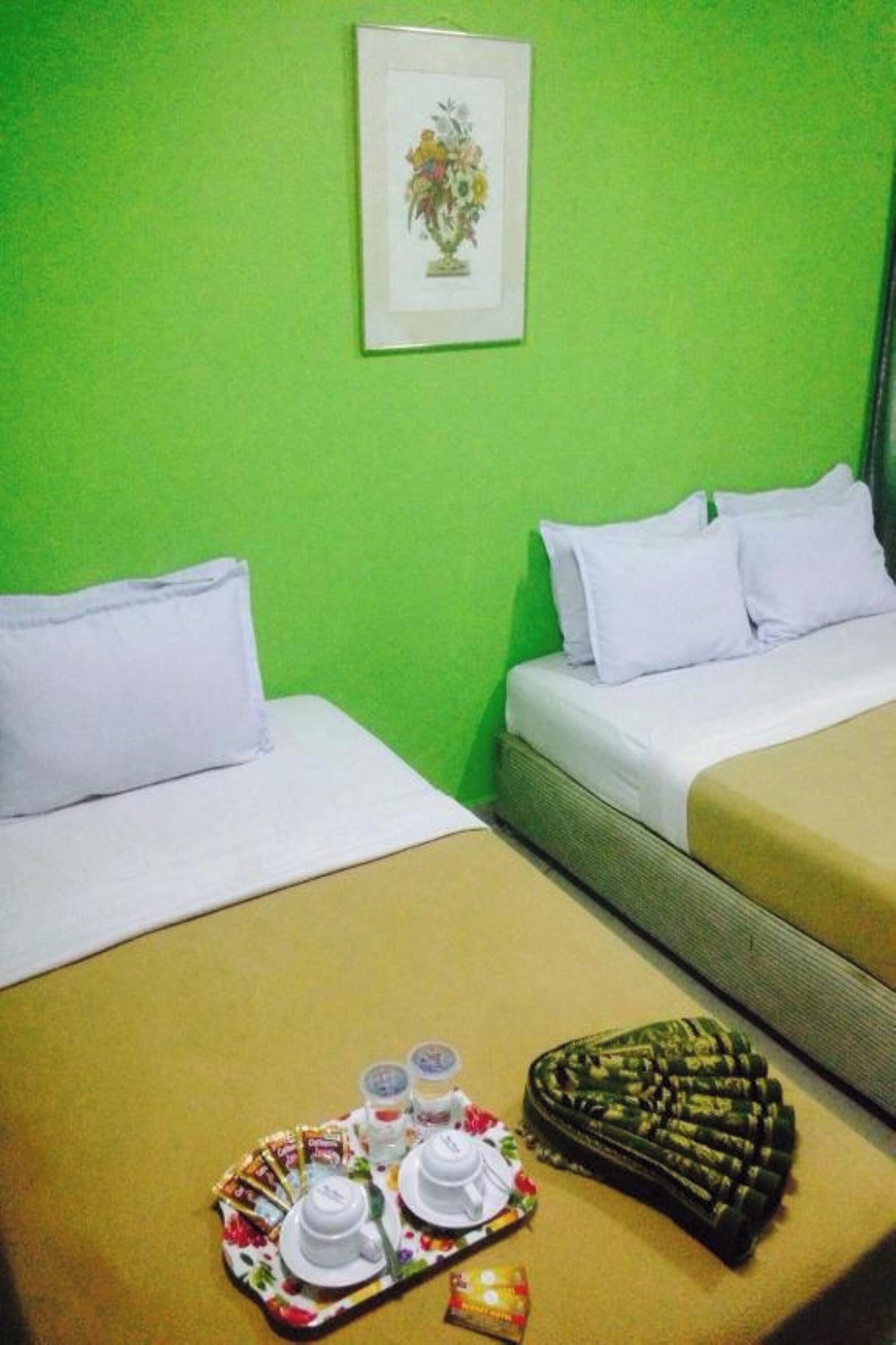 A hotel room with two beds, a green wall, and a framed picture above the left bed.