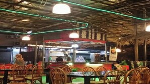 An indoor restaurant with wooden chairs and tables, a thatched roof, and green ambient lighting. - F Hotel Bayan Lepas (George Town)