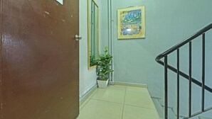 A hallway with a brown door, a potted plant, a framed picture on the wall, and a black railing. - F Hotel Bayan Lepas (George Town)