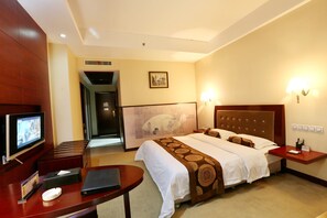 Habitación de hotel con una cama grande, un escritorio con computadora, televisor y una lámpara de pared.