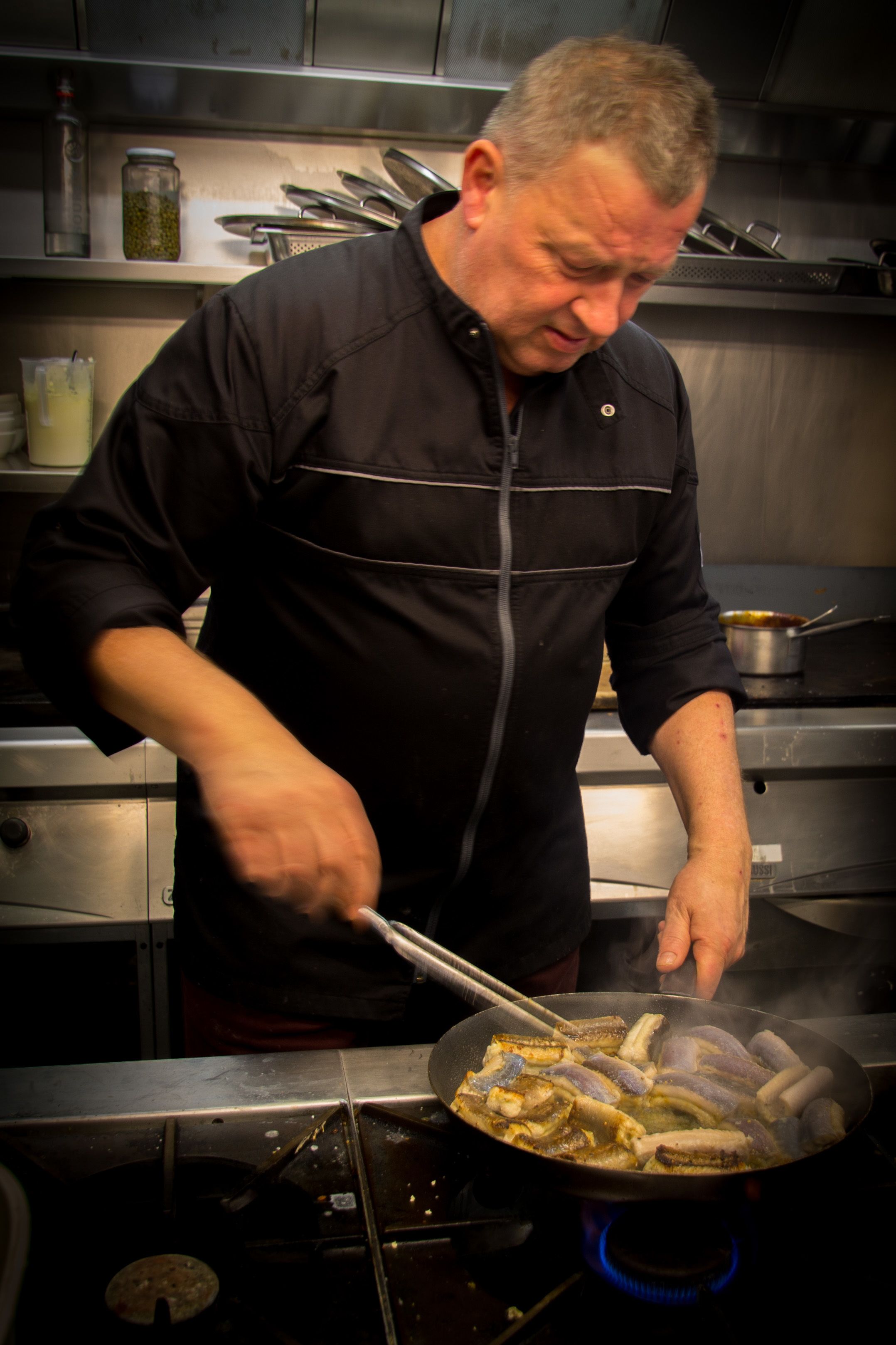 Un chef cocinando en una cocina profesional con electrodomésticos y utensilios de acero inoxidable.
