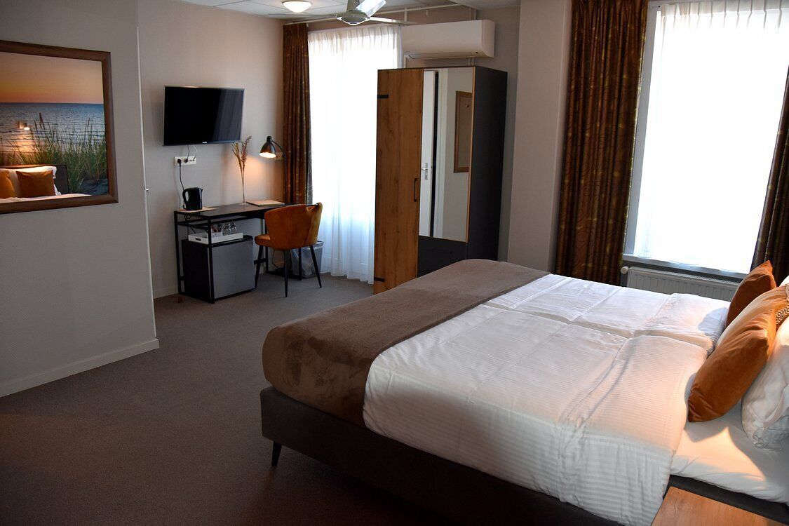 Een hotelkamer met een bed, bureau, stoel, televisie en garderobe.