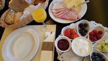 Een ontbijttafel met brood, ham, kaas, fruit en een glas sinaasappelsap.