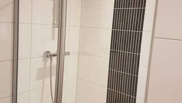 A modern shower enclosure with a glass door and a vertical black tile accent.