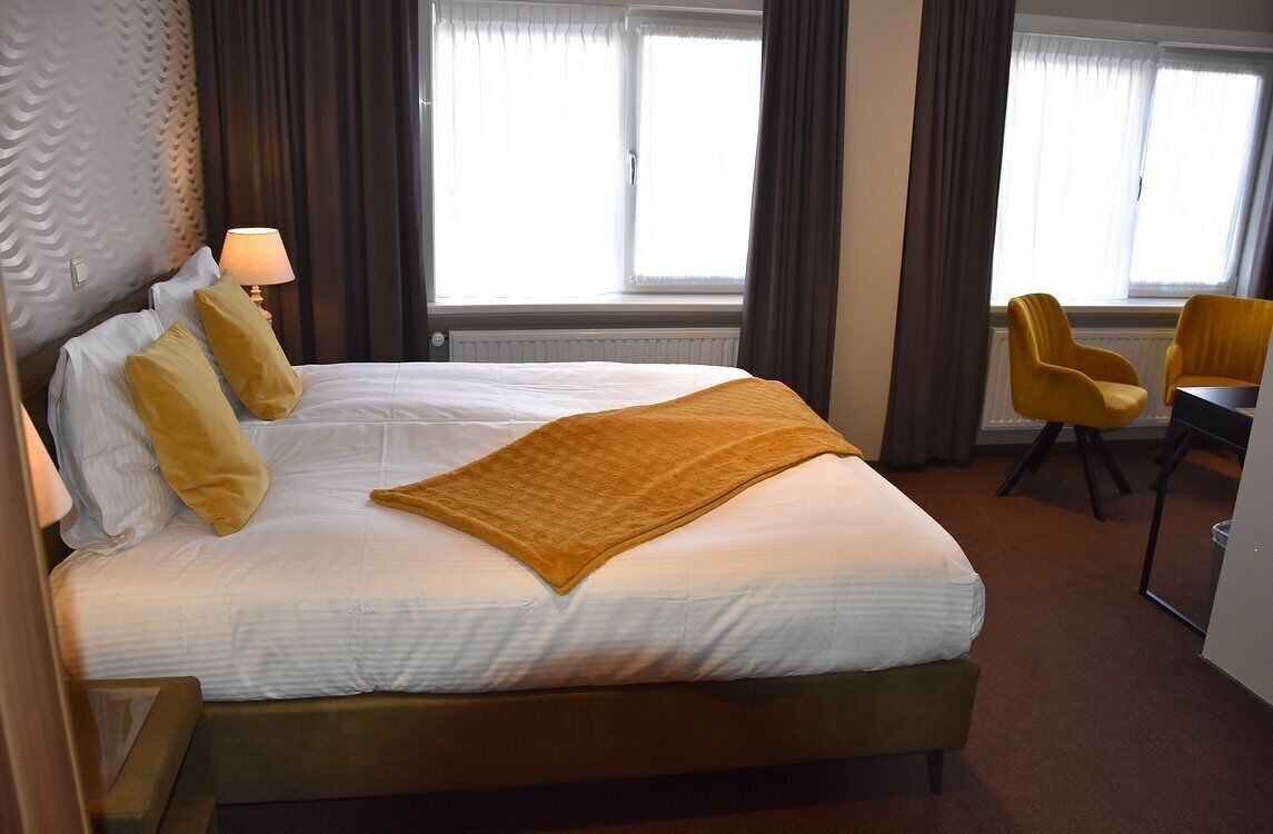 Una habitación de hotel con cama, escritorio, dos sillas y ventana con cortinas.