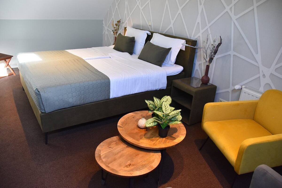 Ein ordentlich eingerichtetes Schlafzimmer mit einem Bett, Nachttischen, einem gelben Sessel und einem kleinen, runden Tisch mit einer Pflanze.