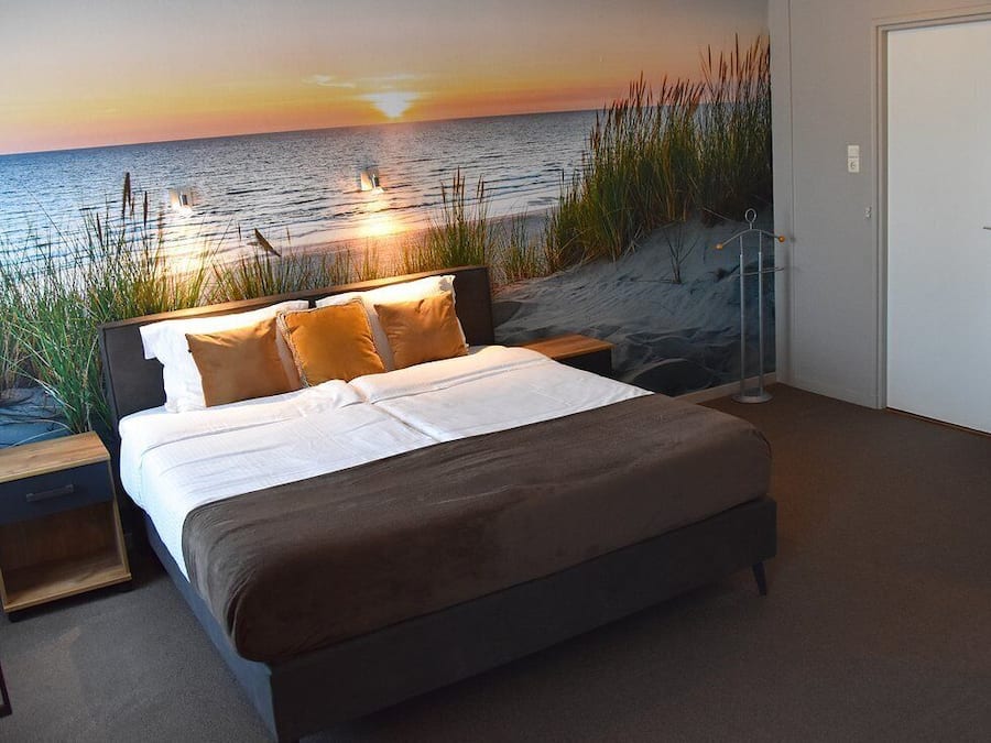 Un dormitorio con cama, mesita de noche y vista al océano al atardecer.