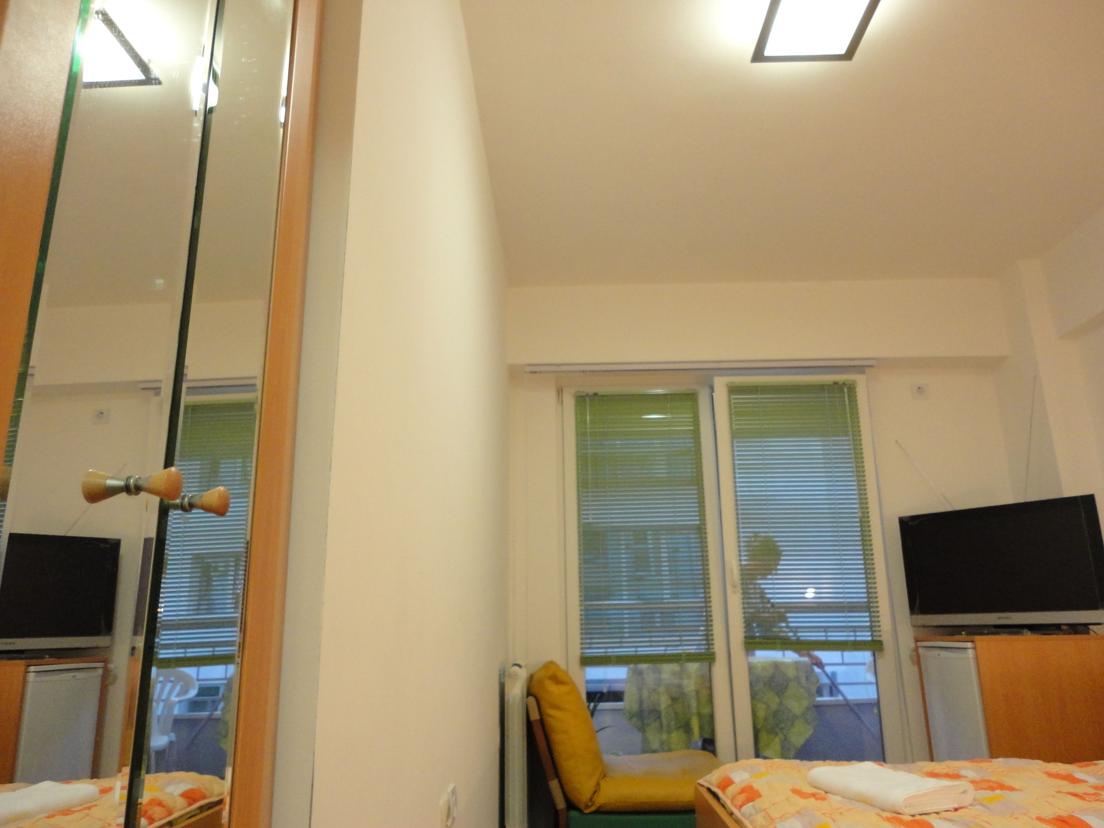 Une chambre d’hôtel avec un lit, une chaise, une télévision et une fenêtre avec des stores.