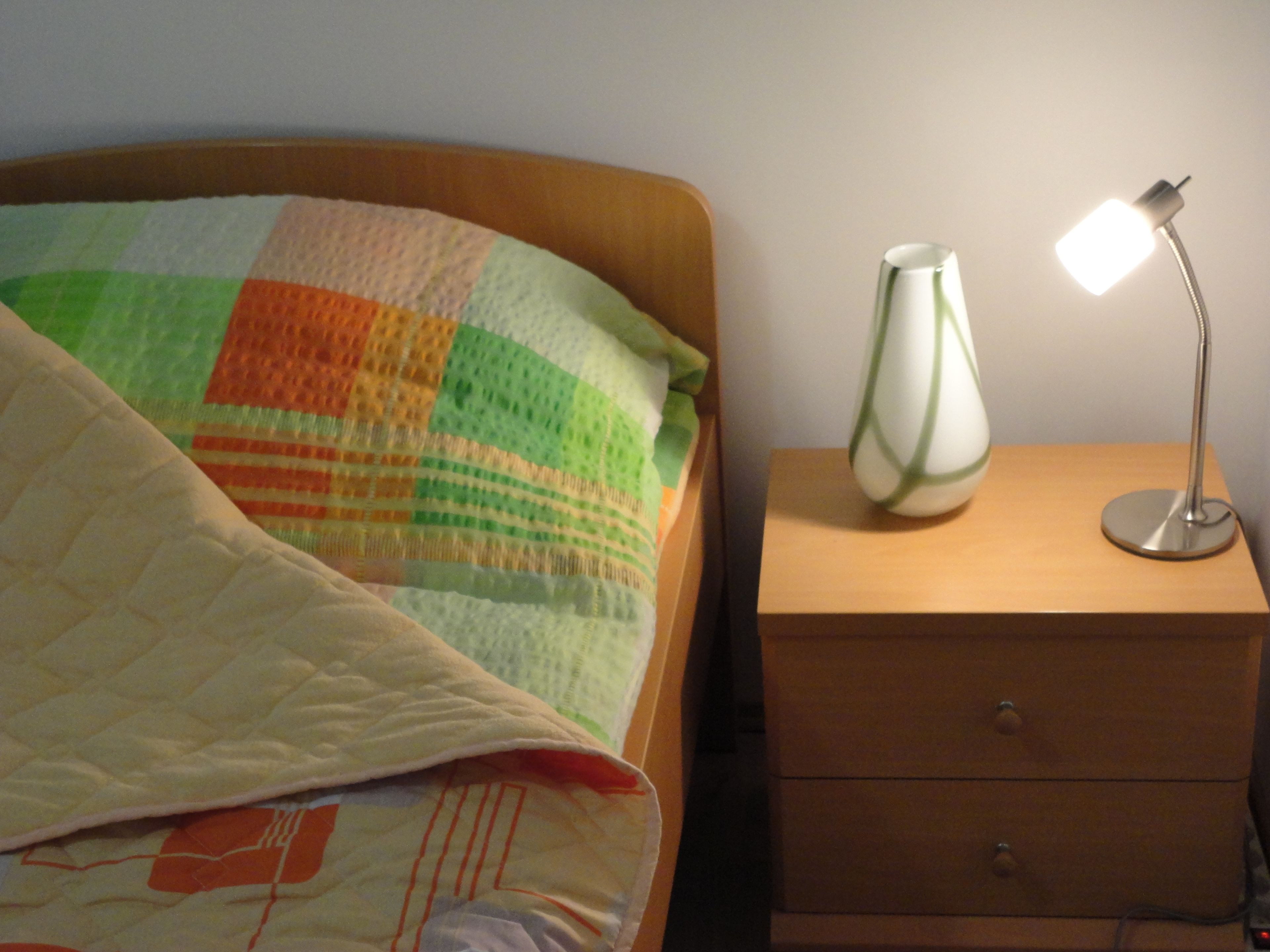 Una cama con un colcha colorida, una lámpara de noche y una mesita de noche con cajones.