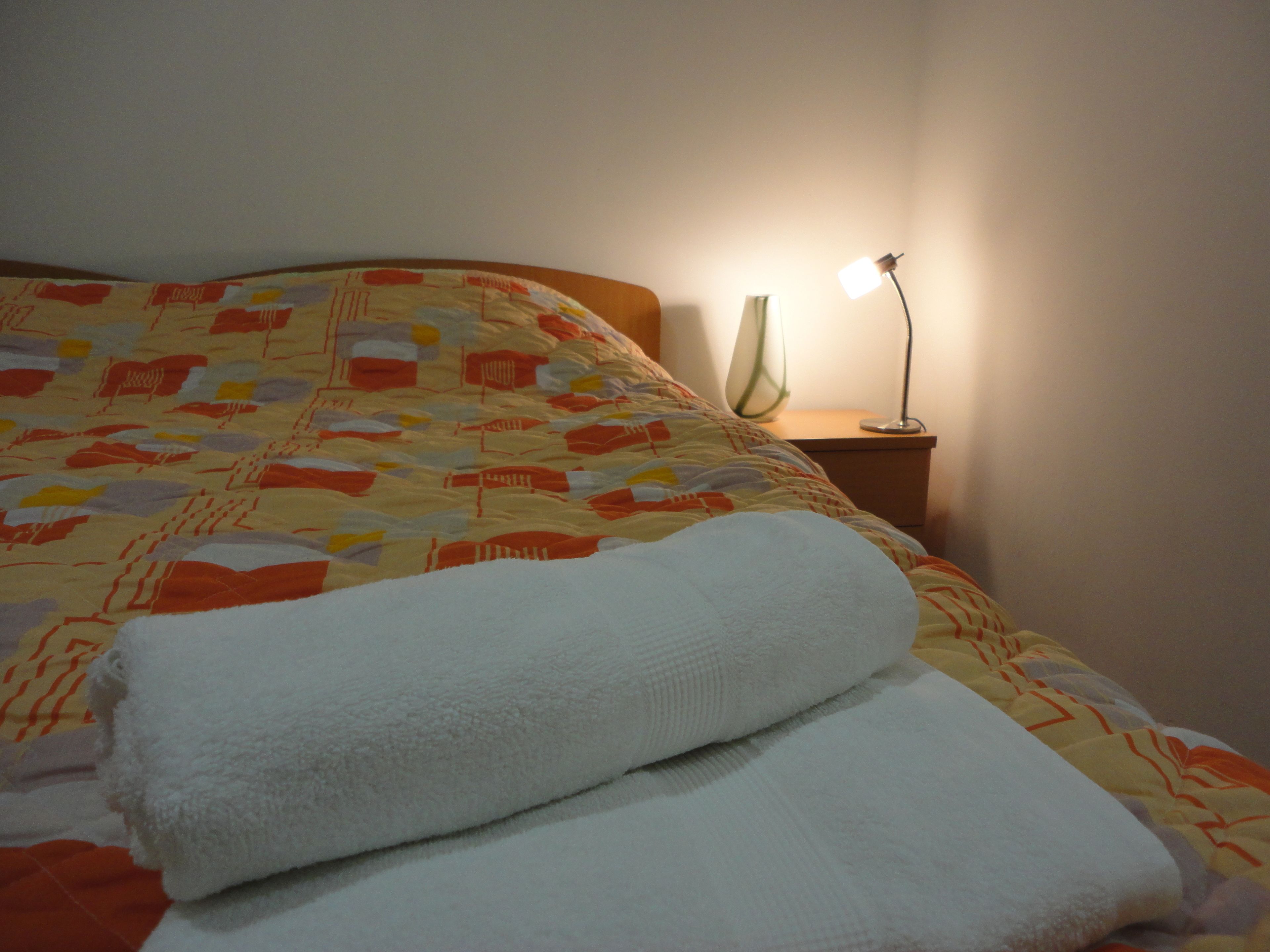 Cama bem arrumada com colcha estampada e duas toalhas brancas dobradas.
