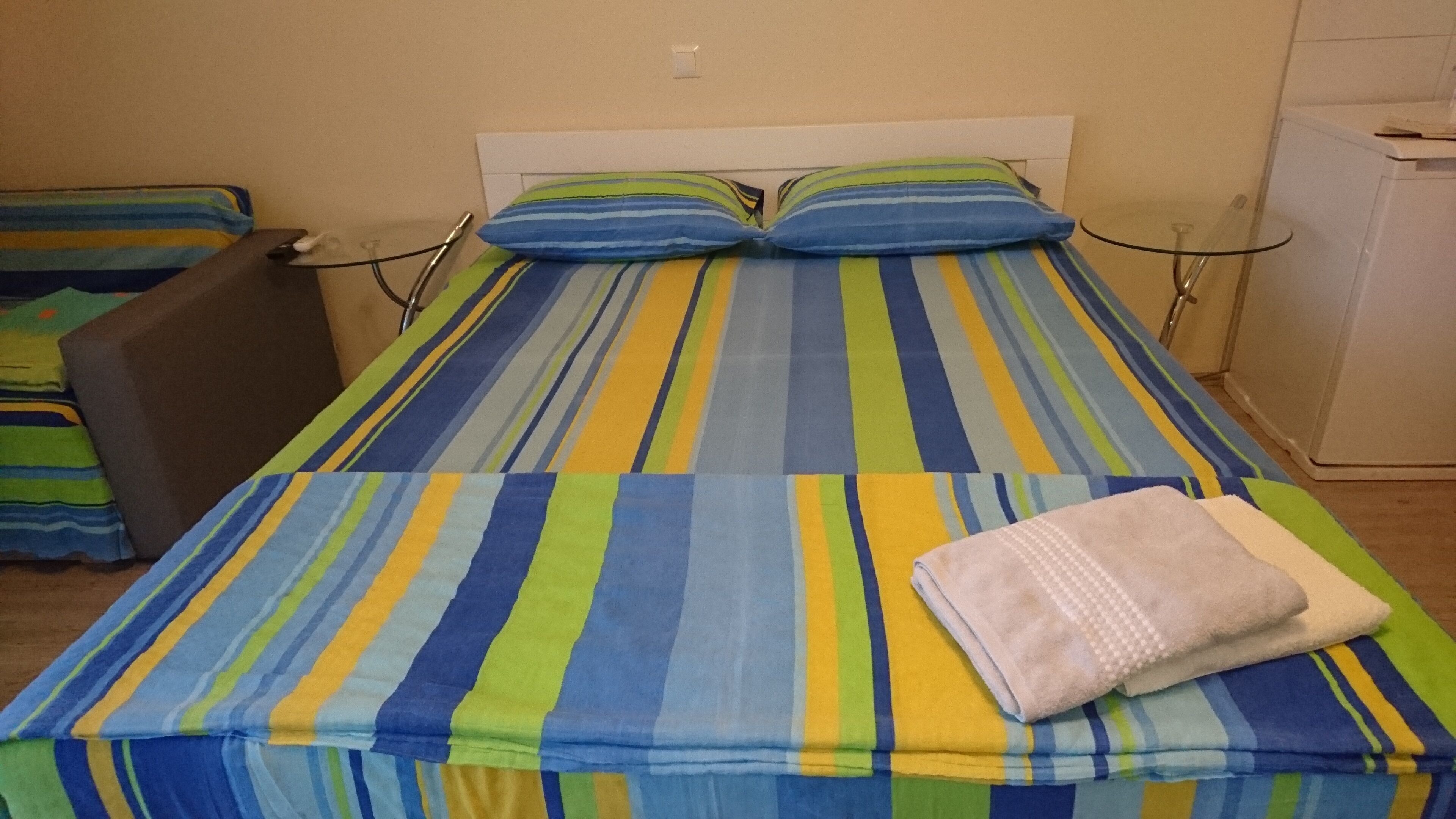 A bed with striped bedding in a room with a white headboard and a small table.