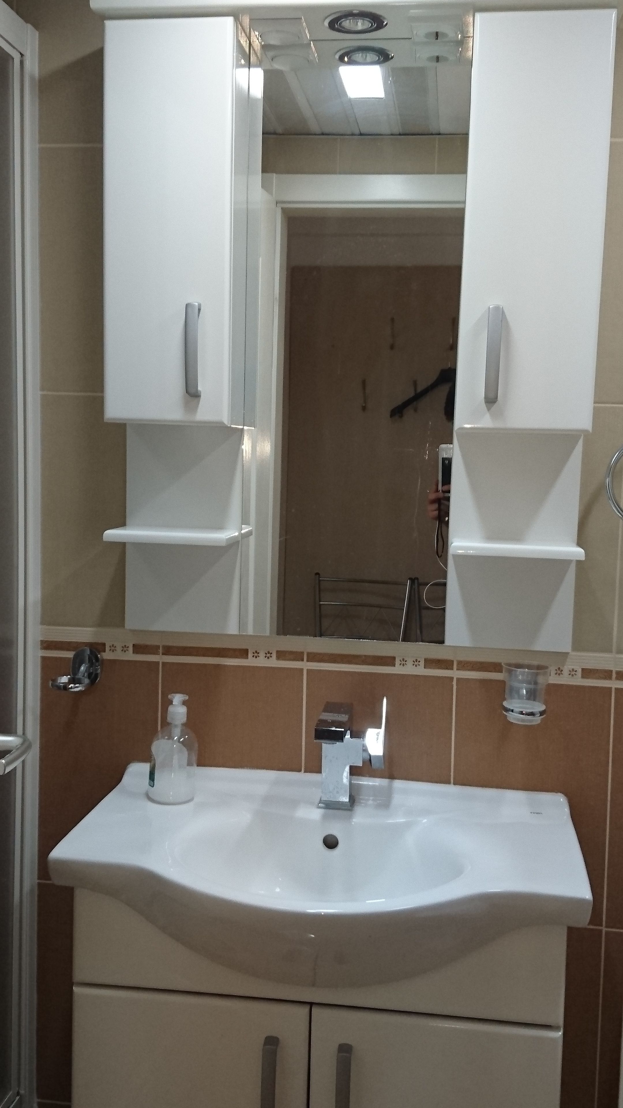 A bathroom with a white sink, mirror, and cabinets. There is a soap dispenser on the sink and a towel rack above it.