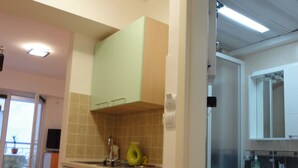 Cocina compacta con armarios verdes, un lavamanos y ventana con vista a un balcón.