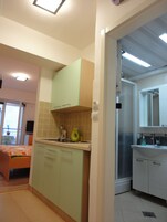 Cocina compacta con armarios verdes, un lavamanos y ventana con vista a un balcón.
