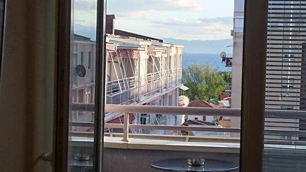 Un balcón con vista a un edificio en construcción, una antena parabólica y una masa de agua al fondo.