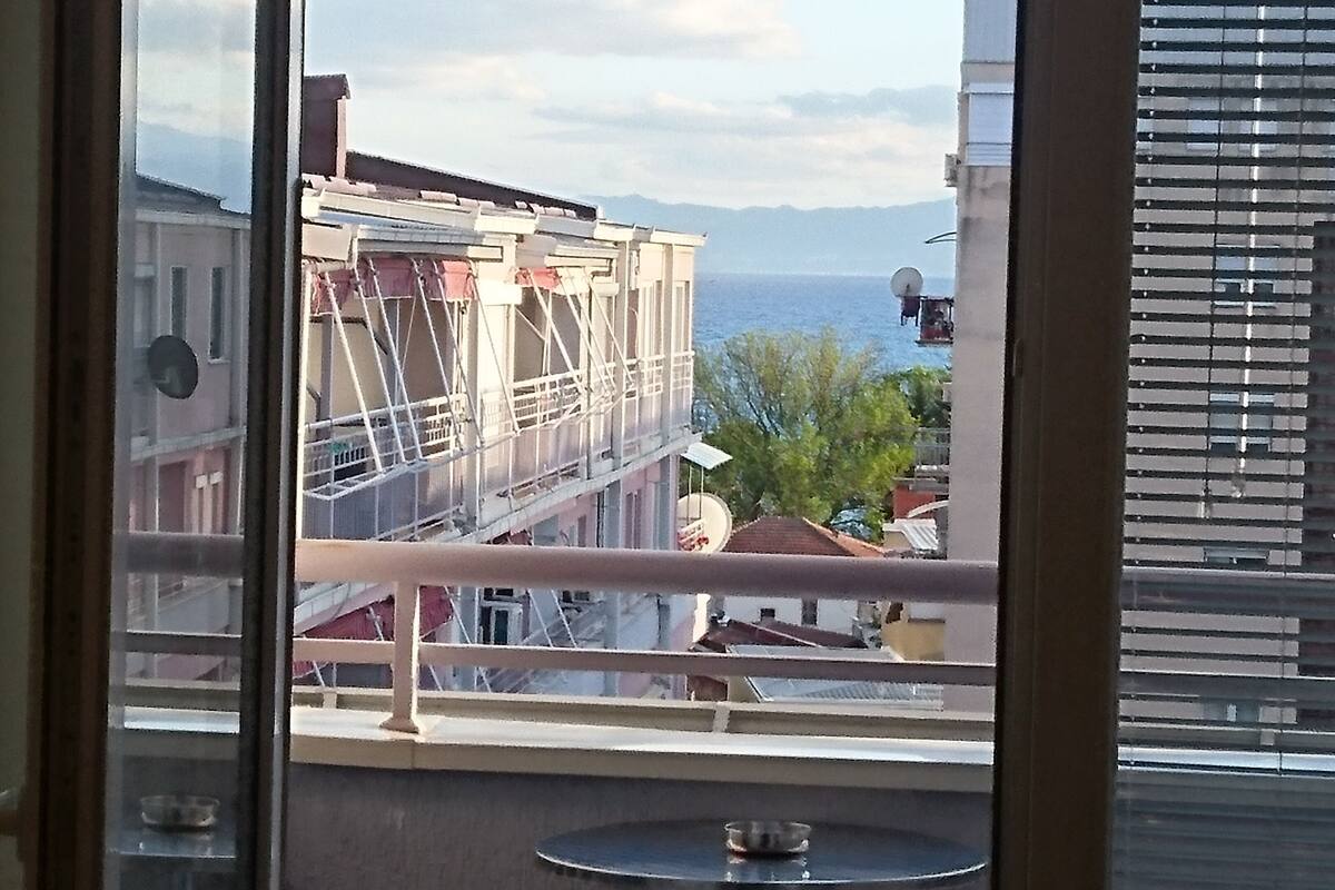 En balkon med udsigt til en bygning i opførelse, en parabolantenne og et vandområde i baggrunden.