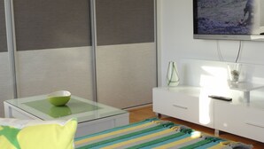 Una sala moderna con una mesa de centro de vidrio, un tapete a rayas, un sofá blanco, un armario blanco y un televisor de pantalla plana montado en la pared.