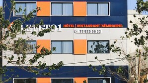 Ein mehrstöckiges Hotel mit modernem Design, mit orange- und blauen Akzenten sowie einer Schilderung, dass es Hotel-, Restaurant- und Seminardienstleistungen anbietet.