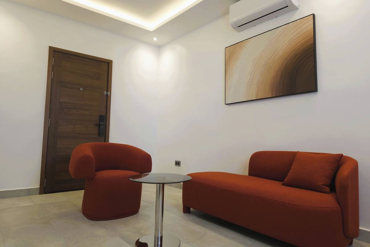 A modern room with a wooden door, a red sofa, a small round table, and a wall-mounted air conditioner.
