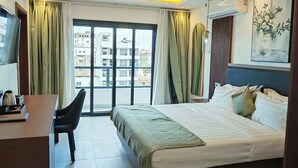 Ein Hotelzimmer mit einem großen Bett, einem Schreibtisch mit Stuhl, einem Fernseher und einem Fenster mit Vorhängen.