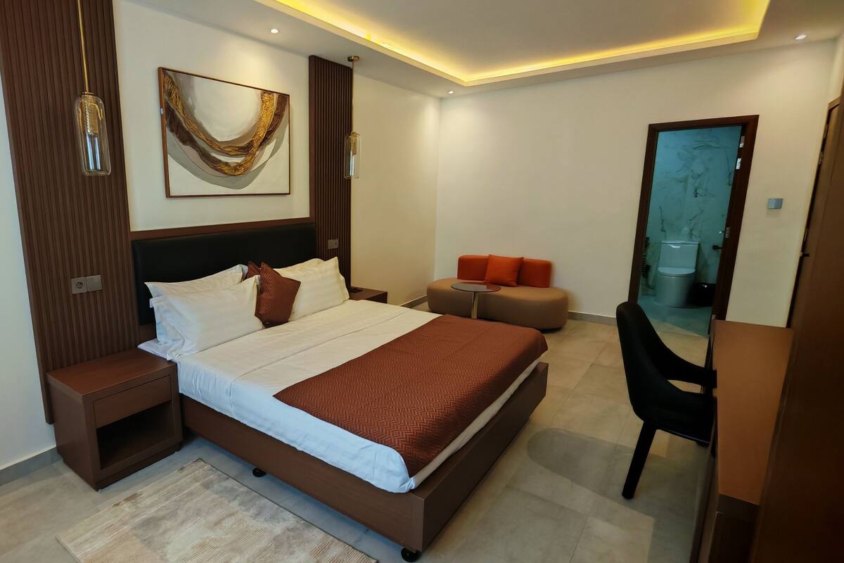 A modern hotel room with a large bed, a bedside table, a mirror, and a small seating area.