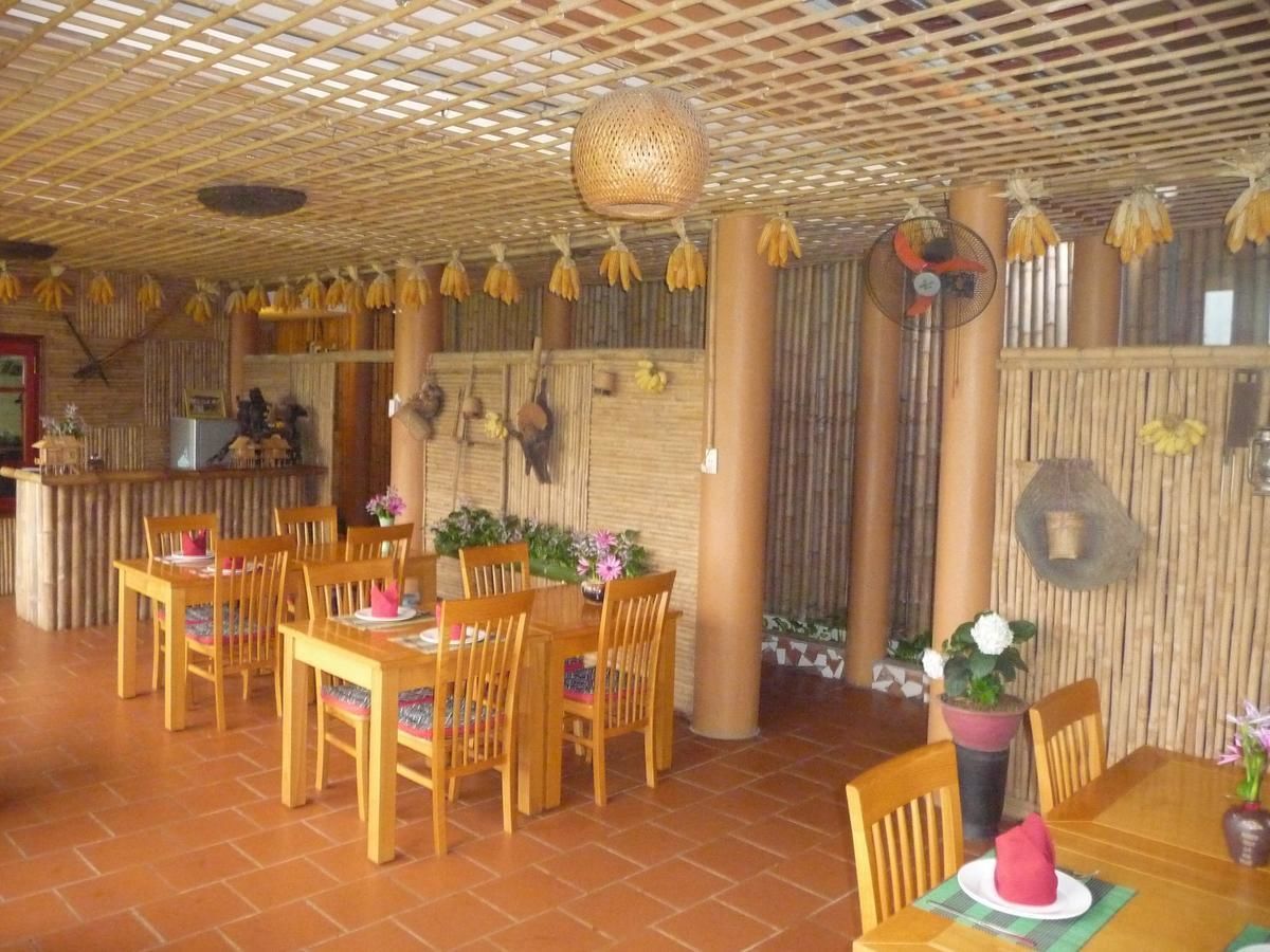 A restaurant with wooden tables and chairs, a bamboo ceiling, and hanging bunches of bananas.