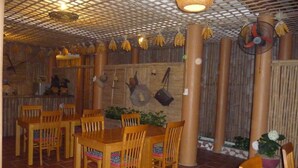 Restaurante com mesas e cadeiras de madeira, piso de azulejos e teto de bambu.
