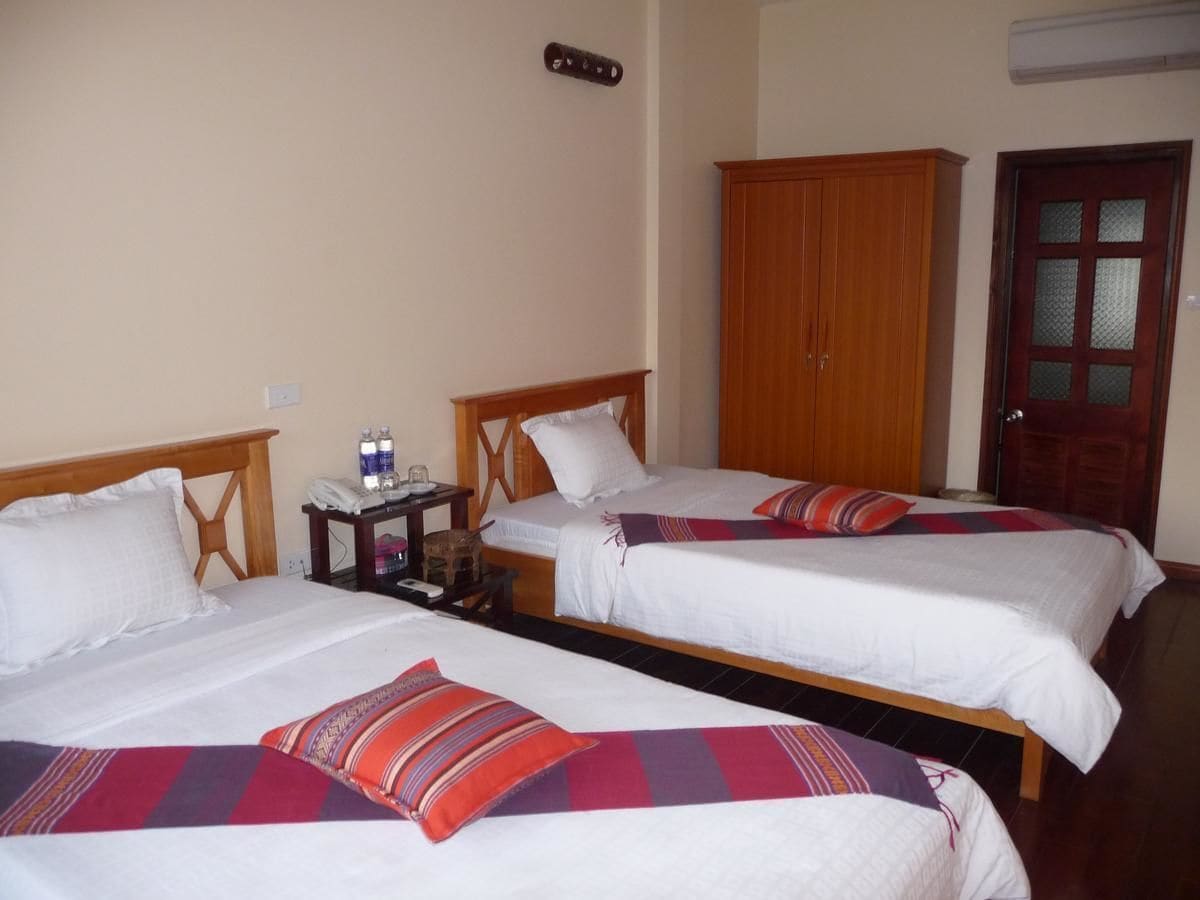 Habitación de hotel con tres camas individuales, cabeceros de madera, un armario y una puerta con panel de vidrio esmerilado.
