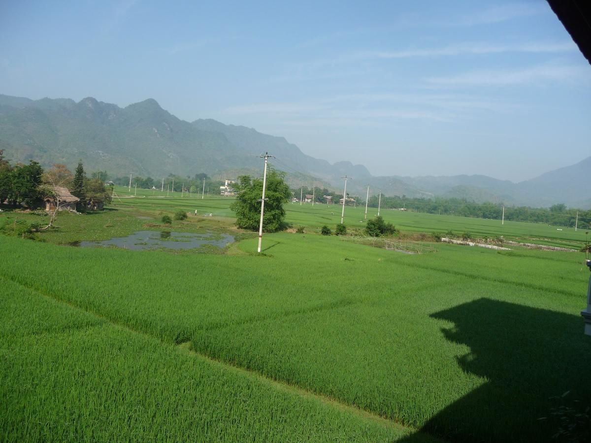 A rural landscape with green fields, a few scattered houses, and distant mountains.