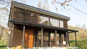 A modern two-story house with a wooden exterior, large windows, and a porch with outdoor seating. - Moon Cabin (Kutchan)
