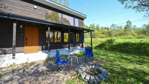 A modern house with a wooden exterior, a porch with blue chairs, and a fire pit. - Moon Cabin (Kutchan)