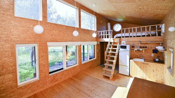 A wooden cabin with multiple windows, a kitchen area, and a loft bedroom. - Moon Cabin (Kutchan)
