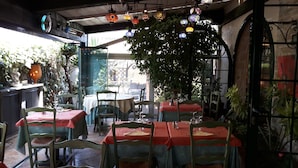 An outdoor dining area with tables and chairs, hanging decorative lights, and potted plants. - Auberge Les Arômes (Grasse)