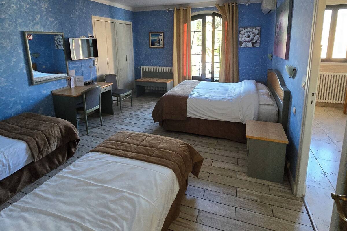 A hotel room with two beds, a desk, a chair, a radiator, and a window with curtains.