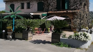 A two-story building with a stone facade, green shutters, and a tiled roof. - Auberge Les Arômes (Grasse)
