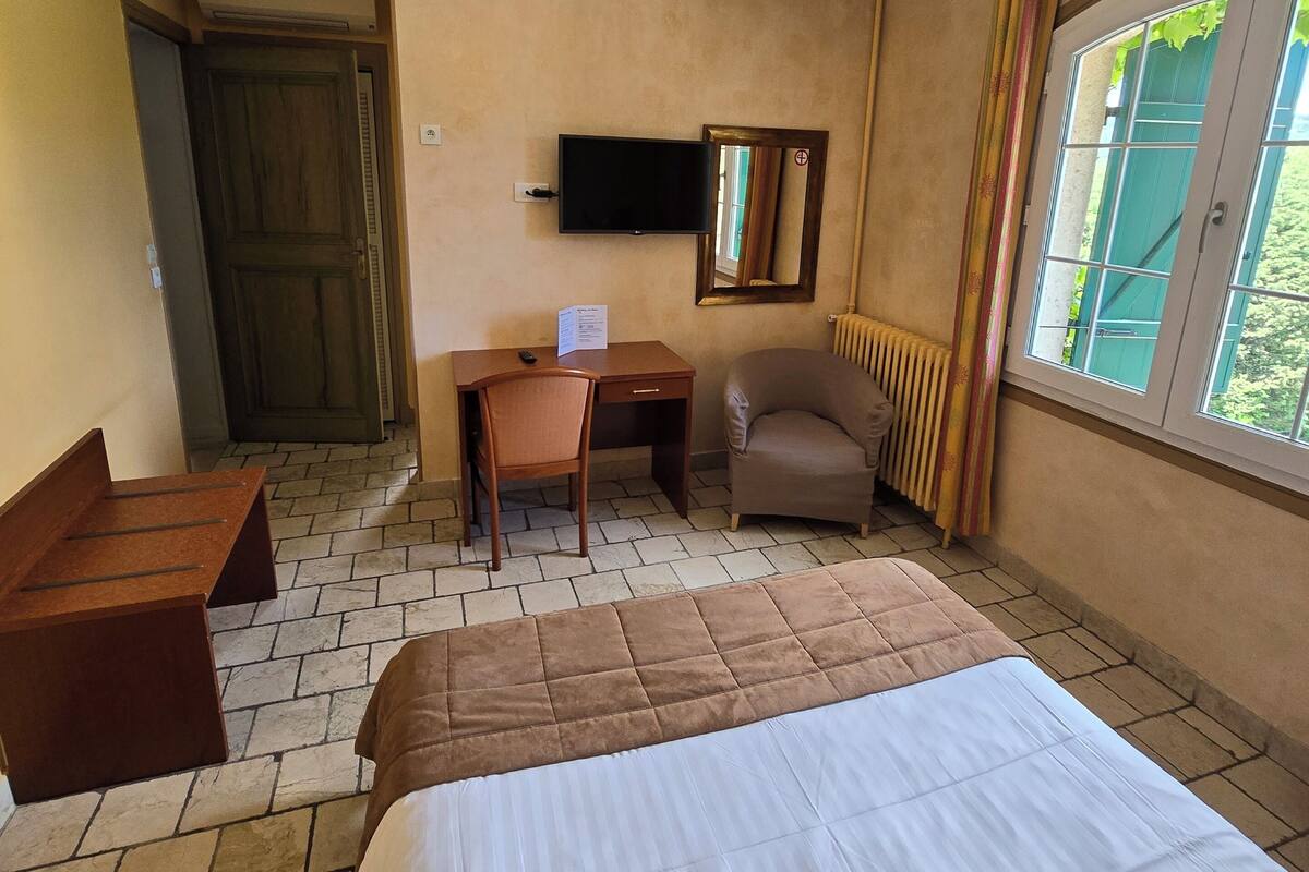 A hotel room with a bed, a desk, a chair, a TV, and a window with curtains.
