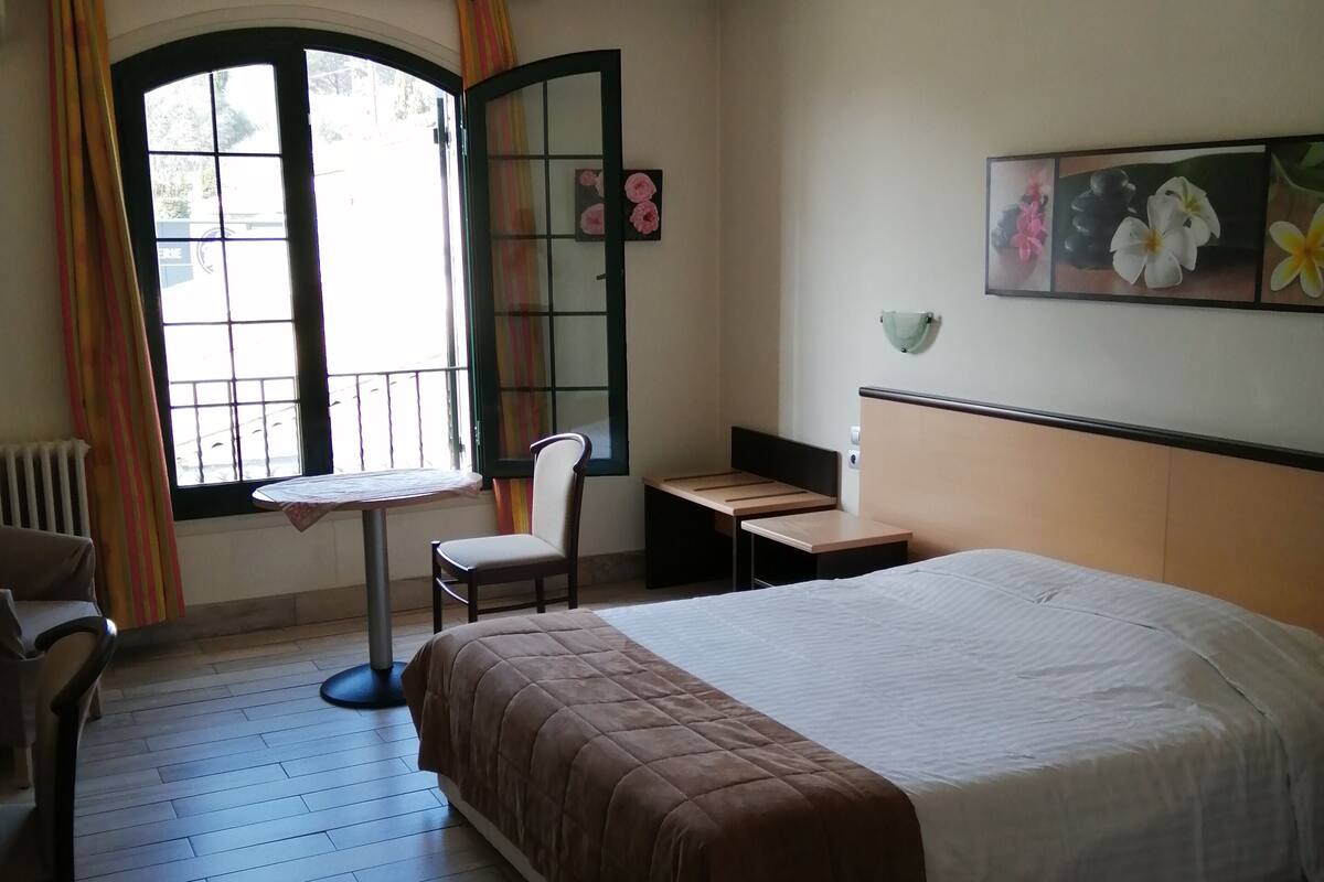 A hotel room with a bed, a desk, a chair, and a window with curtains.