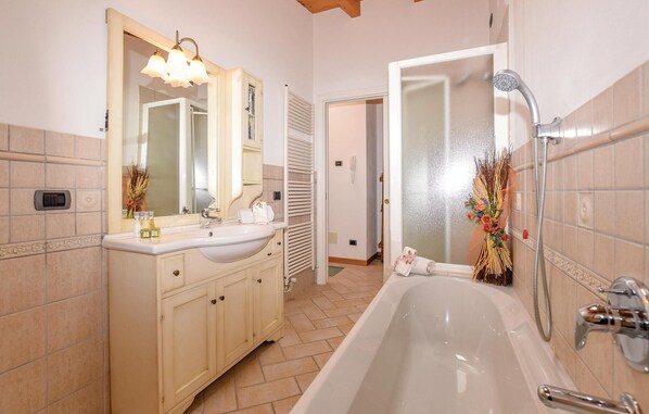 A bathroom with a bathtub, a double sink vanity, a mirror, and a shower.