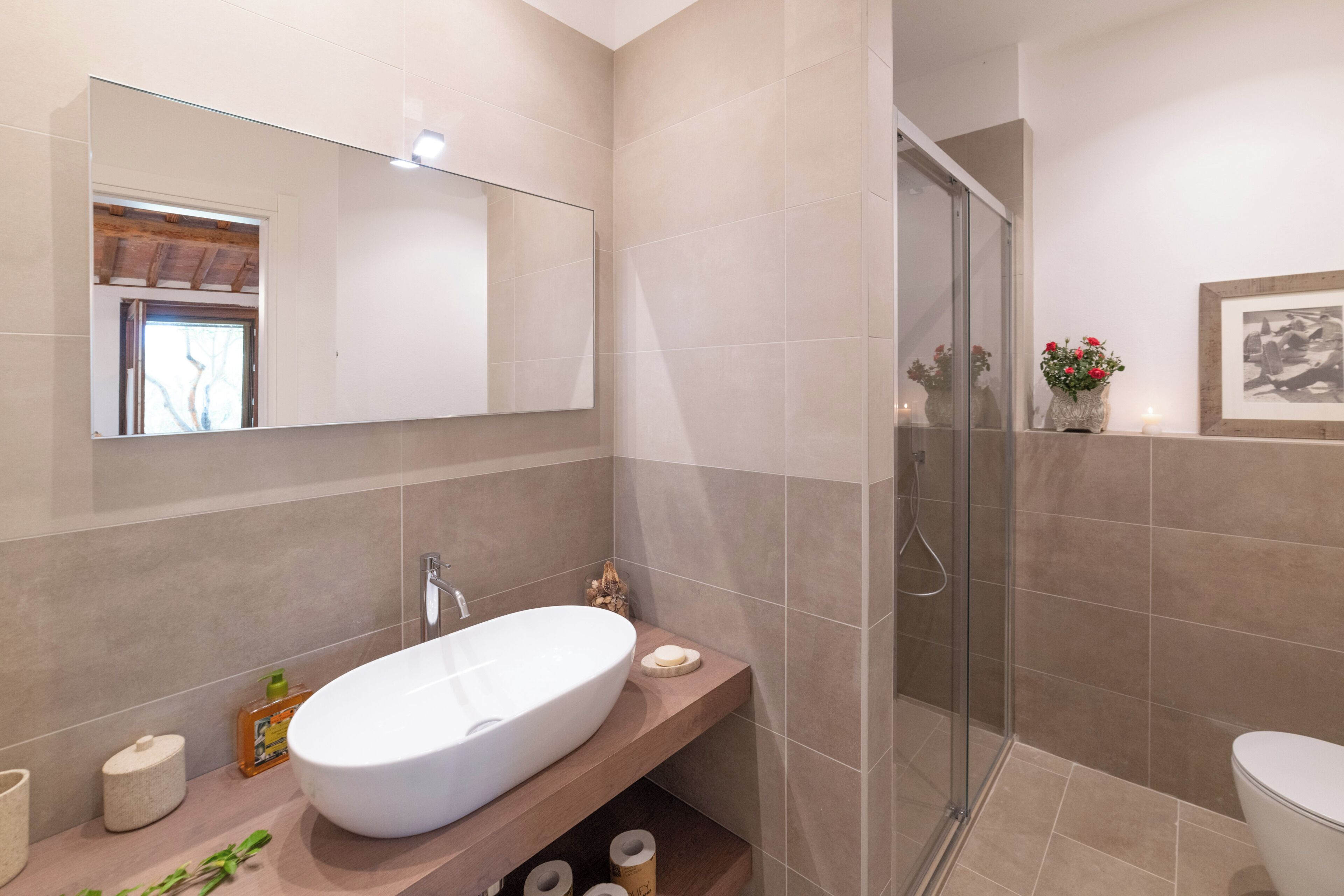Ein modernes Badezimmer mit einem großen Spiegel, einem Waschbecken, einer Dusche und einer Toilette.