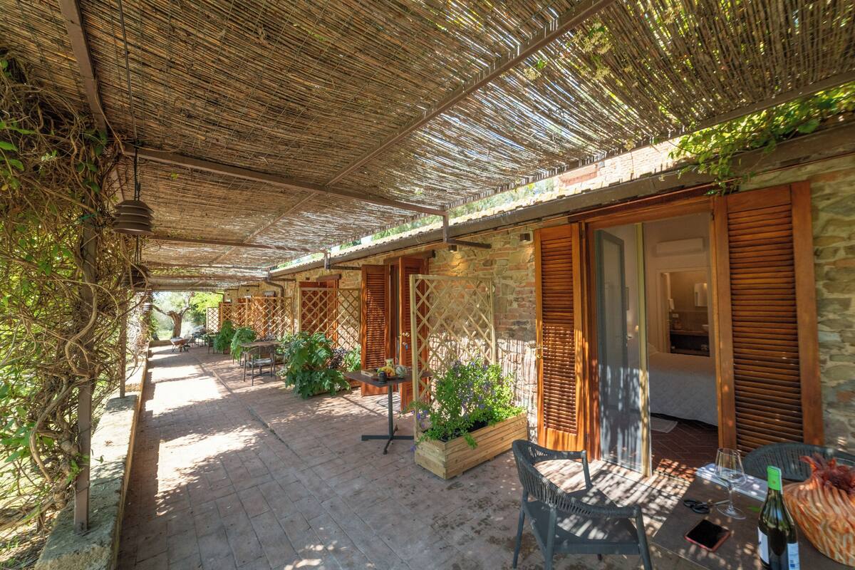 A covered outdoor area with a thatched roof, wooden furniture, and stone walls.