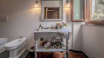 A bathroom with a white sink, a mirror, two wall-mounted lights, a window, and a toilet.